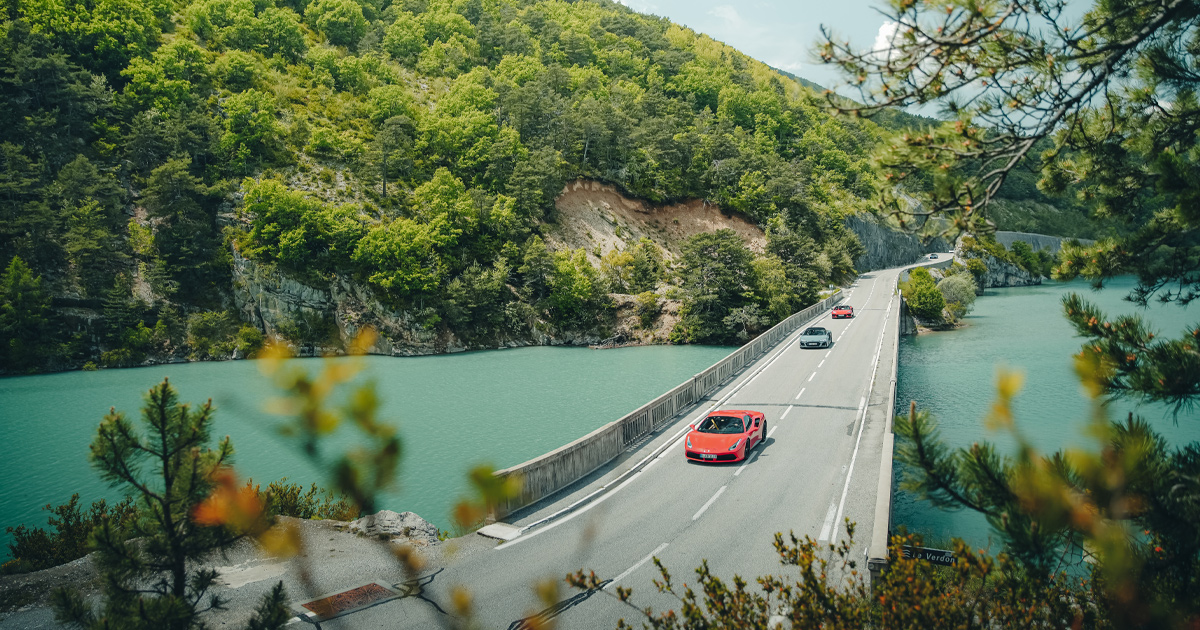 A red Lamborghini leads a convoy of supercars across a bridge in Europe