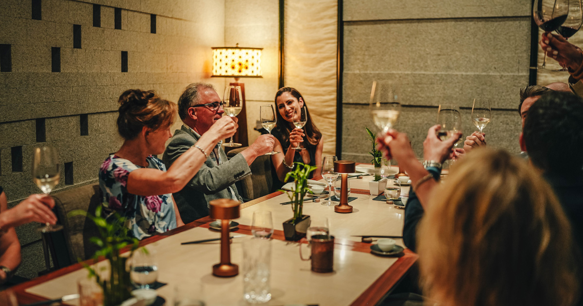 An Ultimate Driving Tours group of guests shares a toast around an elegant dinner table at a fine dining restaurant