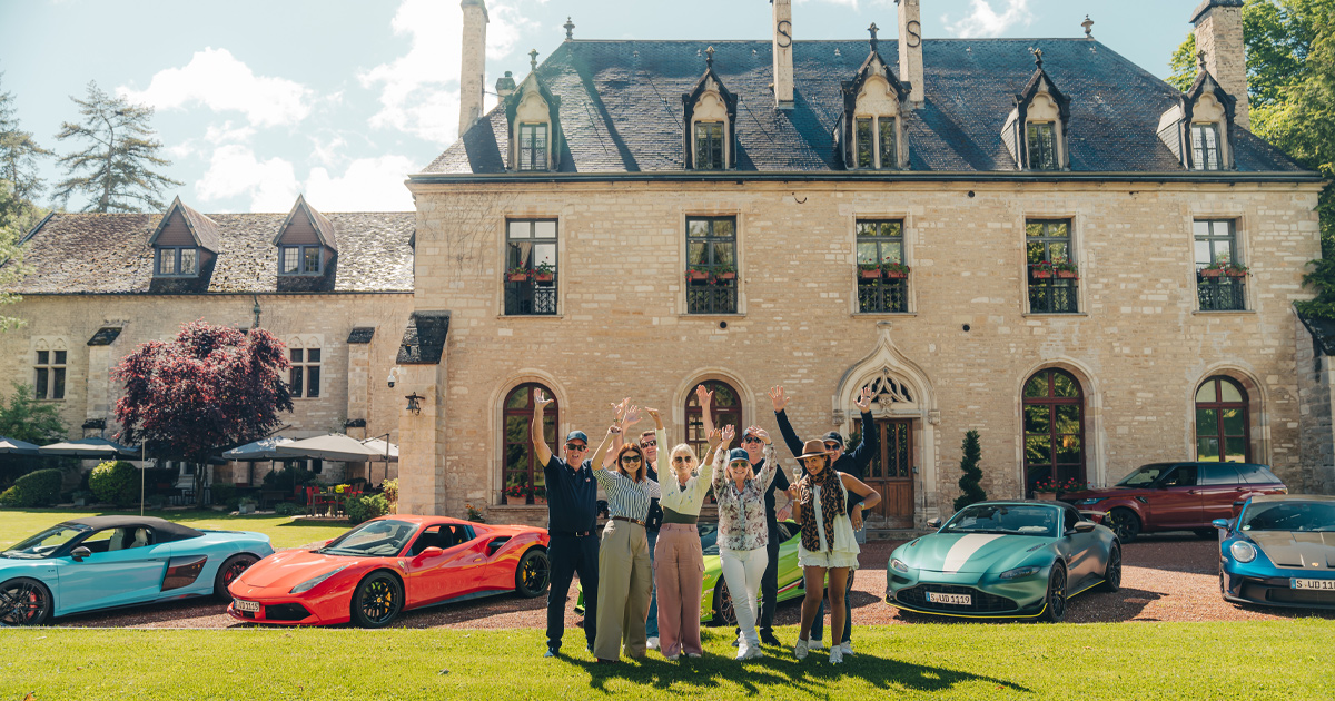 Ultimate Driving Tours guests with hands raised in celebration outside a historic country estate in France