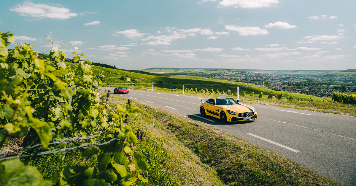 A yellow Mercedes AMG GTR rounding a country bend with vines on both sides of the road