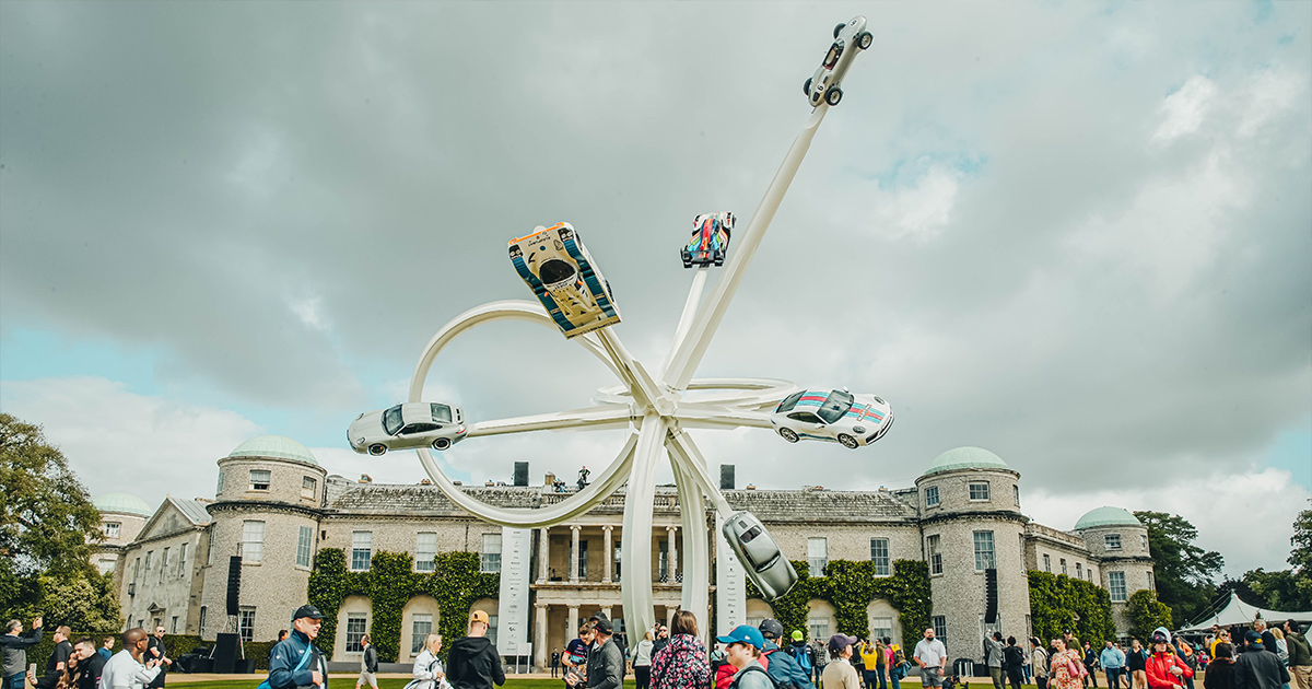 A huge sculpture with long beams with a racing car on each beam in front of Goodwood House
