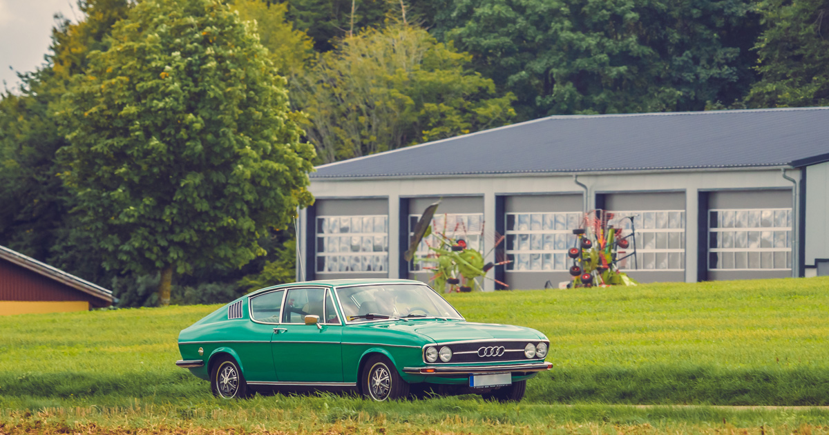 An immaculate green Audi 100 coupe being driven along a country road