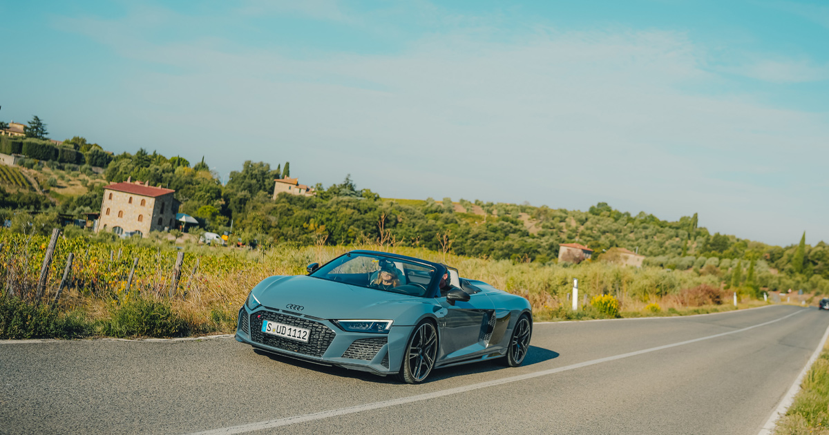 A blue Audi R8 Spyder driving on a country road with top down