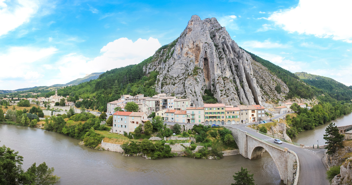 A French riverside town located below a large cliff surrounded by green valleys