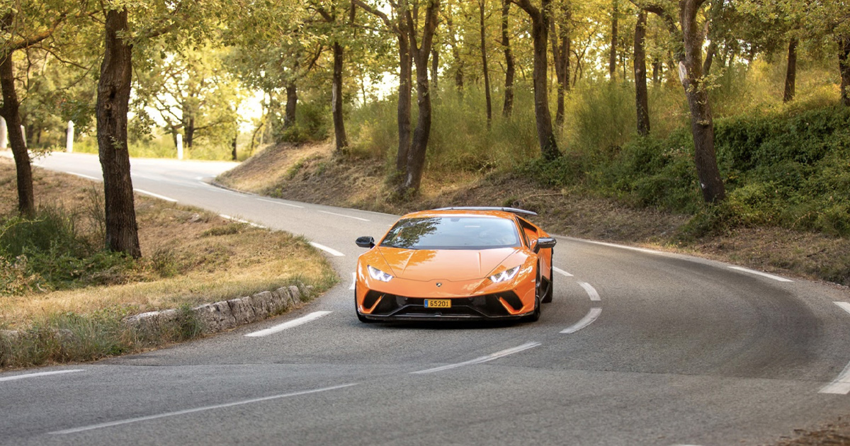 An orange Lamborghini Huracan rounding a forest road bend in France