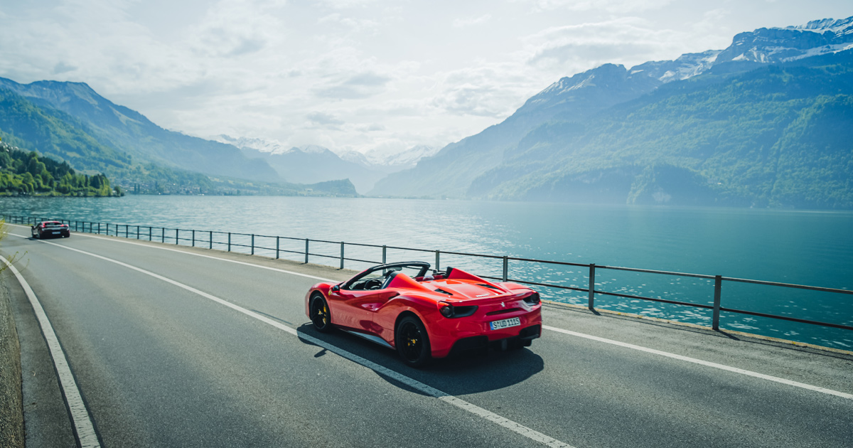 A red Ferrari 488 Spyder driving alongside a Swiss alpine lake.