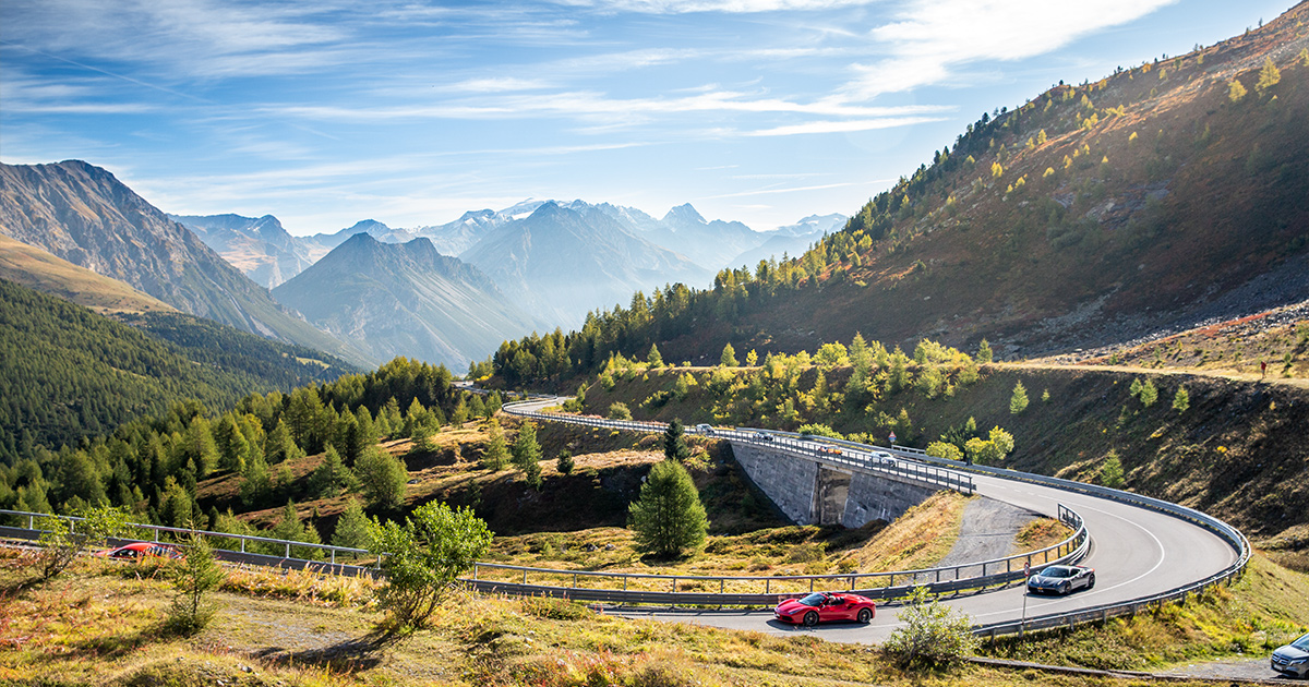 A supercar cruises around a long corner in the mountains on a crisp sunny day