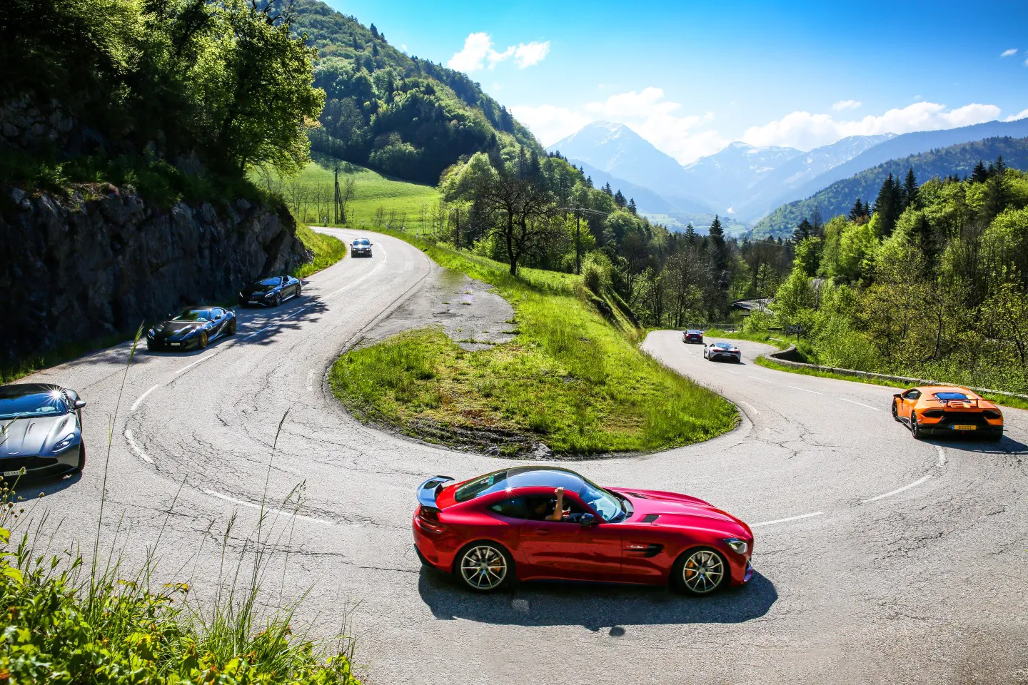 Convoy of supercars driving alpine roads in Europe on a luxury driving tour