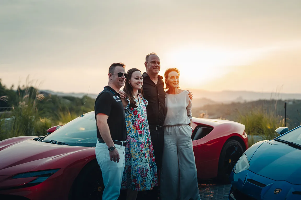Two couples pose happily between their supercars at dusk on an Ultimate Driving Tours adventure