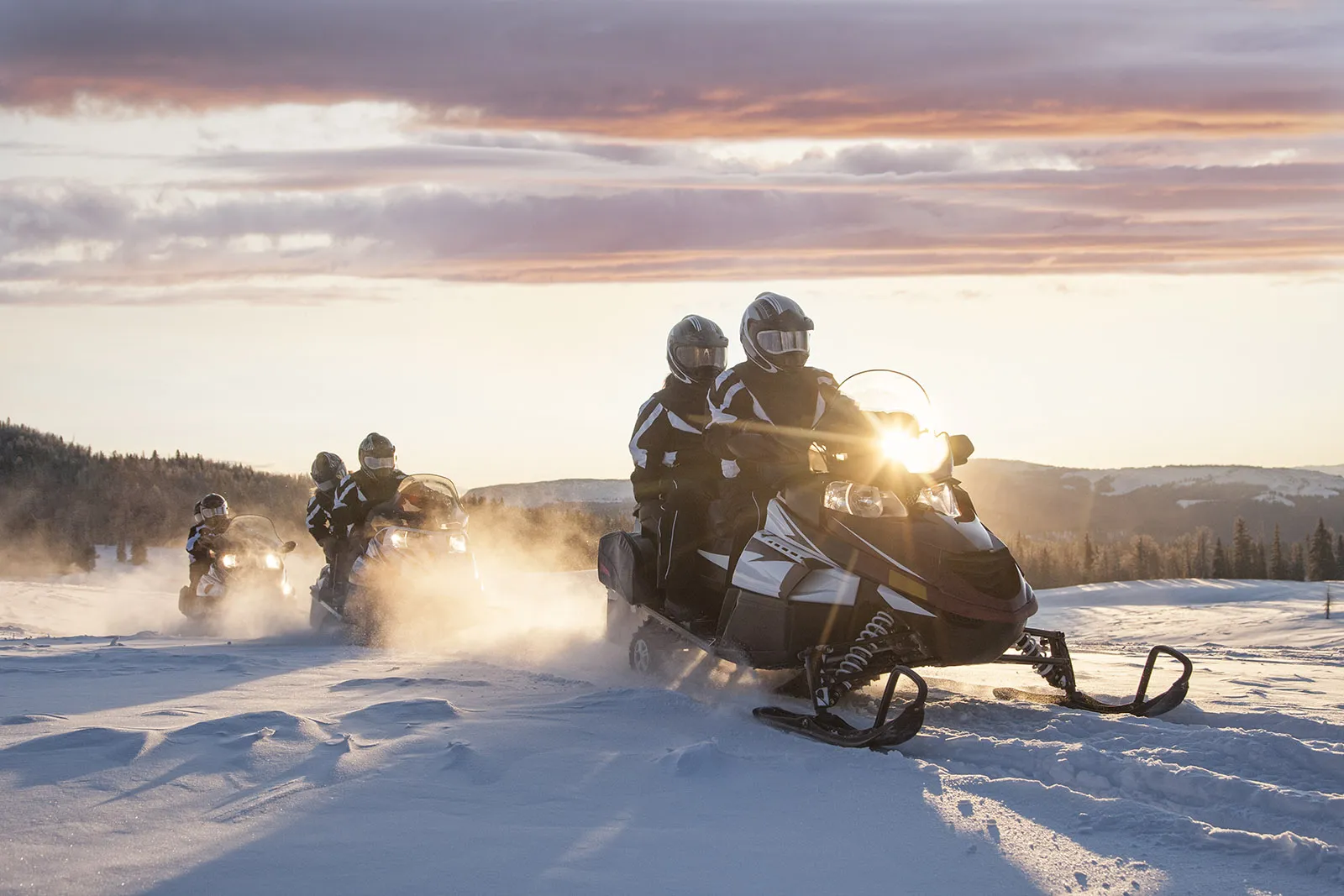 Snowmobiles plowing through the snow at sunset in Swedish Lapland