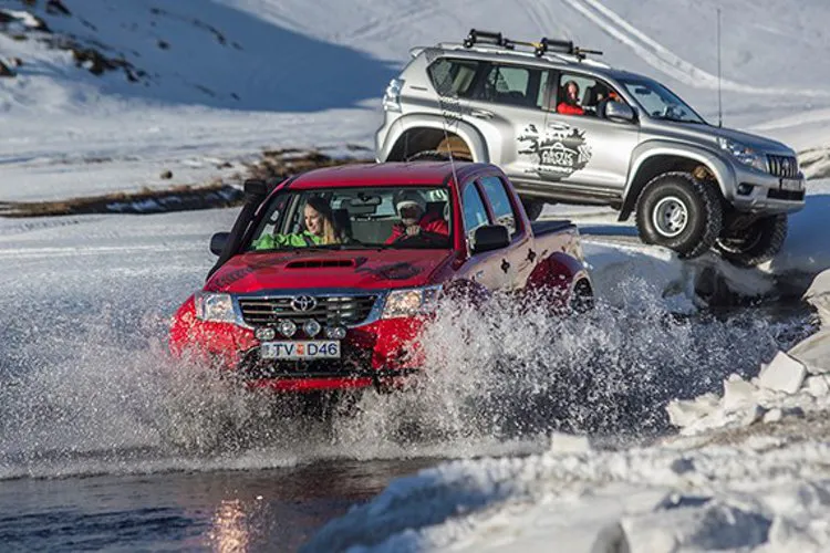 Red and white modified Arctic trucks driving through water in Iceland